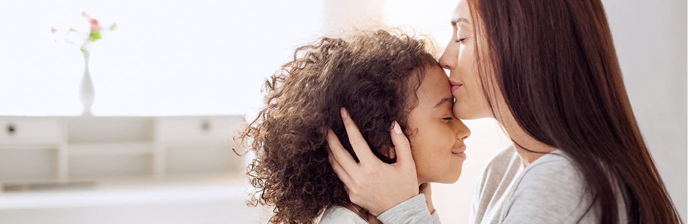 Mother kissing young daughter's head